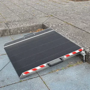 Klappbare Rampe mit rutschfester Oberfläche und rot-weißen Sicherheitsmarkierungen, platziert am Übergang zwischen Gehweg und Straße.