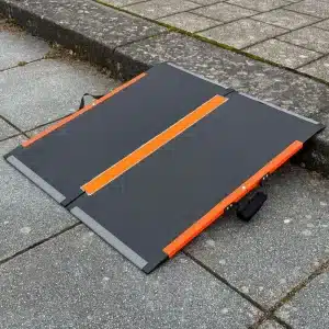 Kohlefaserrampe mit dunkelgrauer Oberfläche und orangefarbenen Akzenten, platziert auf einem Gehweg zur Verbesserung der Barrierefreiheit.